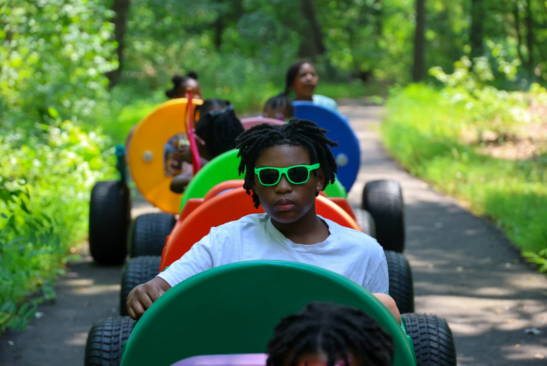 Children riding colorful train cars down a wooded path