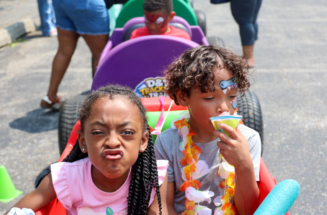 Two kids with face paint riding in colorful D&T Trackless Train cars at an outdoor event