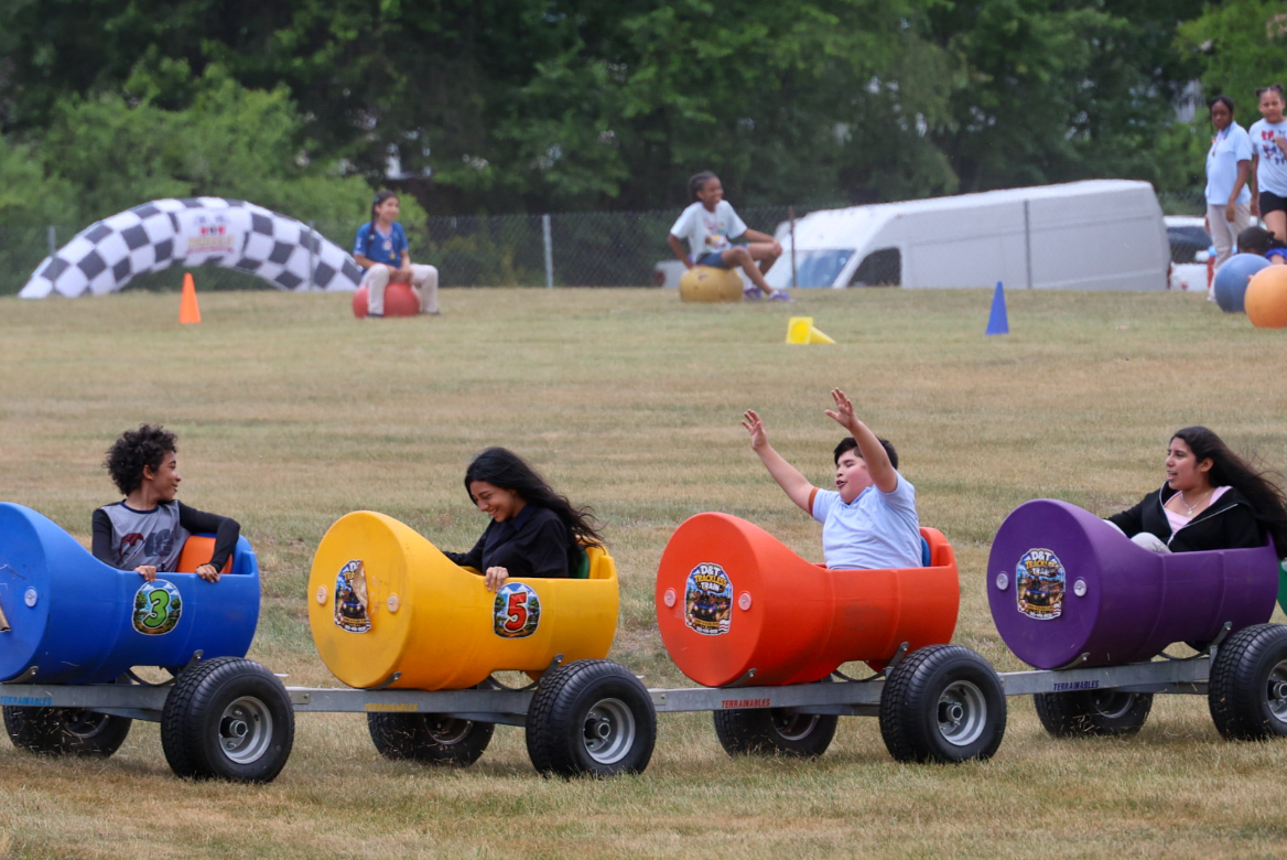Kids waving and smiling while riding the colorful D&T trackless train at an outdoor event